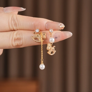 Macro detail of asymmetric gold rocking horse earrings with pearls and pavé zircons