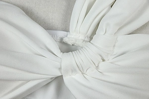 Detailed close-up of knot and pleated texture on white knit dress set for vacation