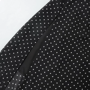 Detail of white polka dots on black chiffon fabric showing quality stitching and hem