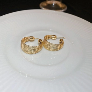 Close-up of golden irregular multi-layer hoop earrings on a white striped plate