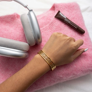 Bracelet jonc évidé en acier doré porté par mannequin sur un pull rose élégant