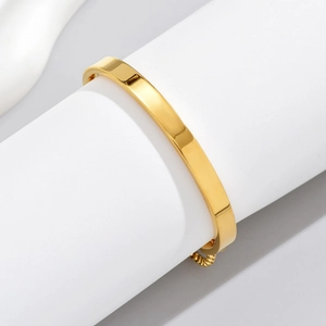 Polished gold adjustable stainless steel open bangle on minimalist white display stand
