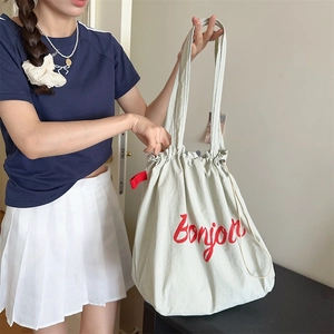 Close-up of beige drawstring tote bag with red Bonjour print shown in a lifestyle setting