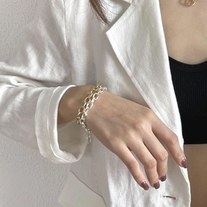 Detail of silver and gold minimalist chain bracelets worn on a wrist over a blazer
