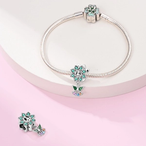 Macro detail of silver snake chain bracelet with green enamel and floral peace pendant