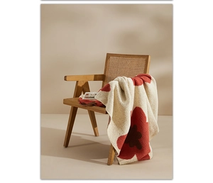 Detail of a beige knitted blanket with red floral patterns on a wooden rattan chair