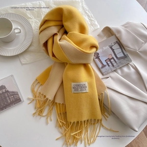Detailed texture of yellow and beige double-sided knit scarf with fringe and brand label