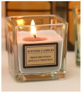 Close-up of a burning white scented candle in a square glass jar with a natural extract label