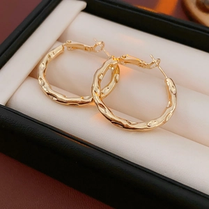 Macro shot of gold geometric hoop earrings with textured hammered finish on white cushion