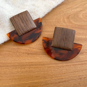 Close-up of geometric square wood and amber resin stud earrings on a textured background