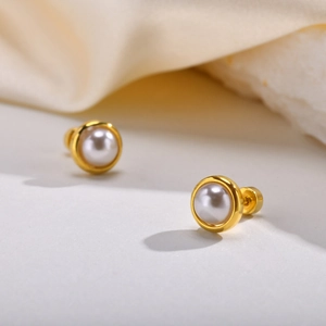 Macro detail of round gold-plated stud earrings featuring elegant white pearls on silk fabric