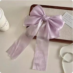 Elegant purple sheer mesh bow hair clip with long ribbons on a decorative wooden tray