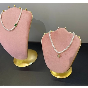 Pink velvet jewelry display stands showcasing pearl necklaces with green emerald pendants