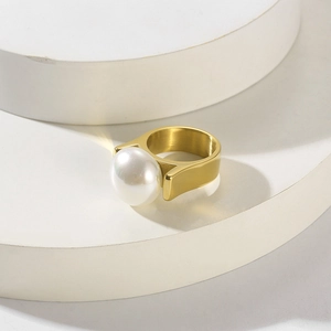Detail eines vergoldeten Edelstahlrings mit großer Muschelperle auf weißem Treppenpodest