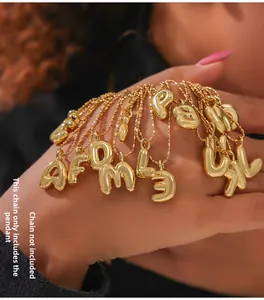 Detail of gold balloon letter pendants held by hand, showing shiny metallic finish
