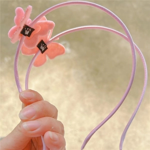 Close-up of two pink satin bow headbands for girls held against a soft outdoor background