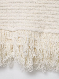 Vue détaillée de la maille blanc crème et des finitions à franges de l'ensemble