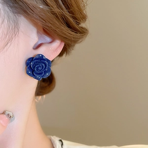 Gros plan d'une boucle d'oreille rose bleu foncé sur un modèle aux détails floraux