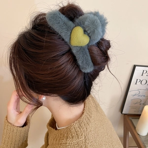 Detailed view of gray plush heart hair claw clip styled on woman's hair in cozy setting