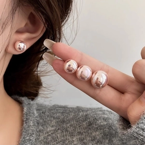 Rose gold round pearl stud earrings for women shown on ear and held by hand