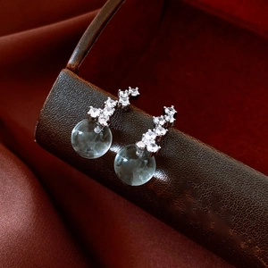 Detailed macro view of zircon-studded round pendant earrings on dark silk background