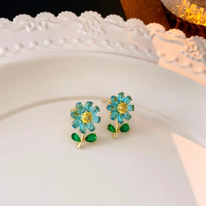 Nahaufnahme der goldenen Blumenohrringe mit blauen Blüten auf einem weißen Keramiktablett