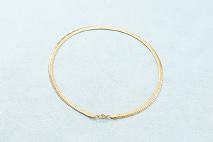Detailed view of the flat golden snake chain necklace on a soft textured background