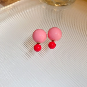 Detail of pink and red double-sided ball stud earrings on a textured tray surface