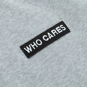 Gros plan du patch brodé 'WHO CARES' sur le sweat-shirt en maille grise pour femme
