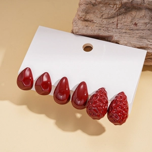 Detailed macro shot of three pairs of deep red acrylic teardrop and textured stud earrings