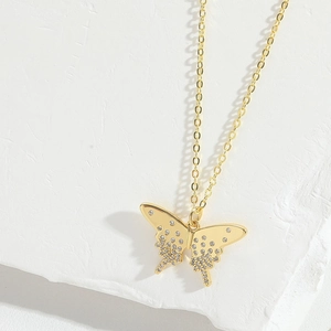 Close-up of a gold butterfly pendant necklace with sparkling rhinestones on white stone