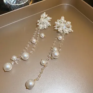 Elegant long tassel earrings with white pearls and crystal beads on a gold tray
