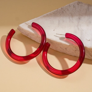 Macro detail of red translucent resin C-shaped hoop earrings on natural stone
