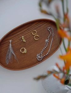 Composizione di gioielli minimalisti in oro e argento su vassoio ovale in legno