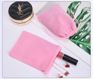 Pink velvet drawstring jewelry pouches on white desk with earrings and lipstick