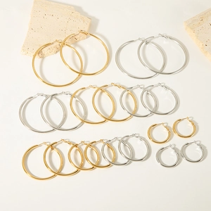 Set of gold and silver stainless steel hoop earrings in various sizes on white stone