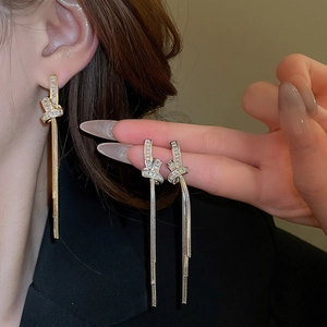Macro detail of gold plated knot tassel earrings with zircon stones worn by a model