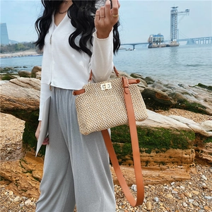 Detail of straw shoulder bag with leather trim and gold twist lock on beach rocks