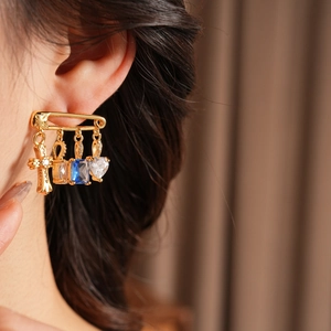 Close-up of a model wearing a gold safety pin earring with zircon cross and heart charms