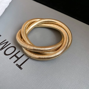 Detailed close-up of golden triple-intertwined spiral metal bracelet with ribbed texture