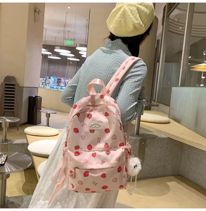 Pink strawberry print backpack on model showing back view in a cozy cafe setting