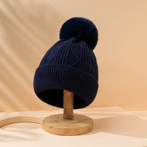 Detail of navy knit beanie featuring a fluffy pom-pom and thick textured pattern