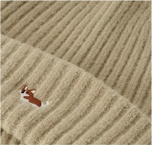 Close-up of thick beige ribbed knit hat featuring a small corgi embroidery detail