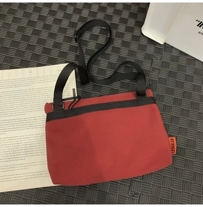 Detailed view of red nylon messenger bag with black strap and orange logo label