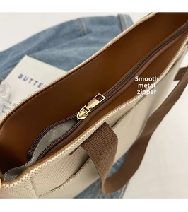 Close-up of golden metal zipper and brown leather trim on beige canvas tote bag