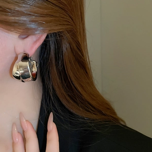 Macro view of wide silver-toned twisted metal hoop earring worn by a model