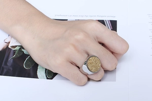 Detail view of a silver stainless steel ring with a round golden druzy top on a finger