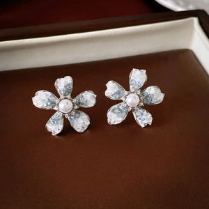 Detail of flower stud earrings with blue crystals and a pearl center on leather