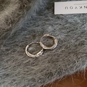 Detail of silver huggie earrings with micro-pave crystal accents on plush fabric