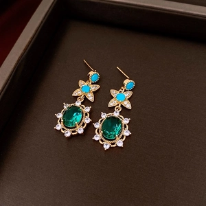 Detail of gold-plated pony earrings with oval emerald stone and clear crystals